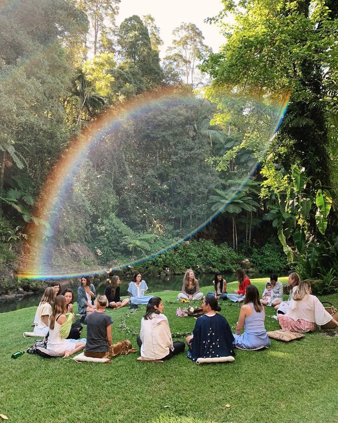 Círculo de meditación junto al río bajo un arcoíris